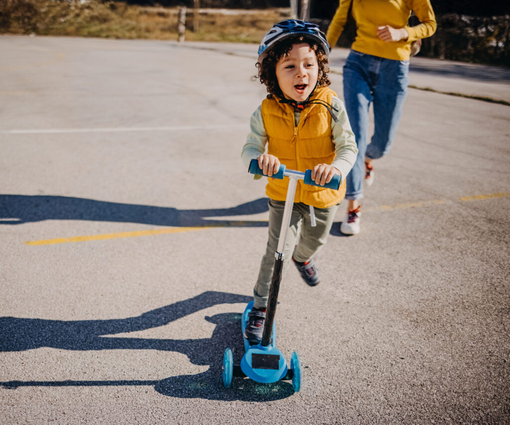 Child wearing a helmet rides on a scooter.