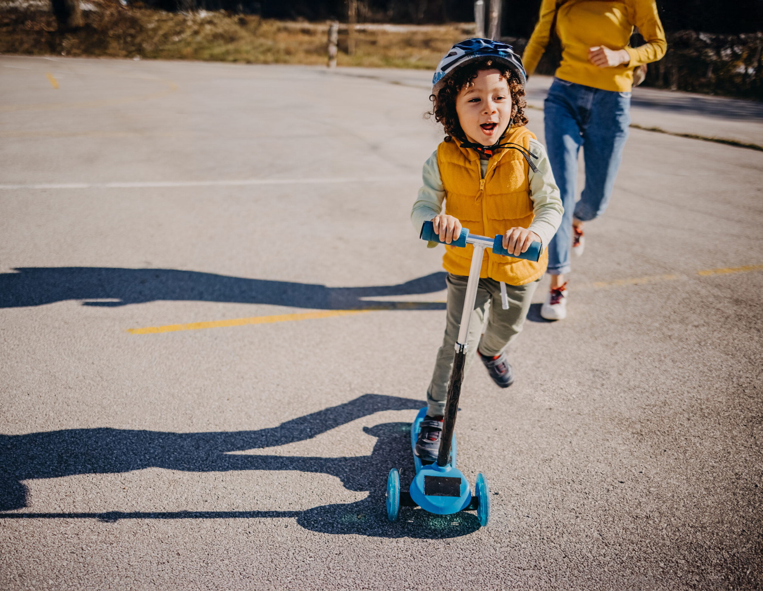 Child wearing a helmet rides on a scooter.
